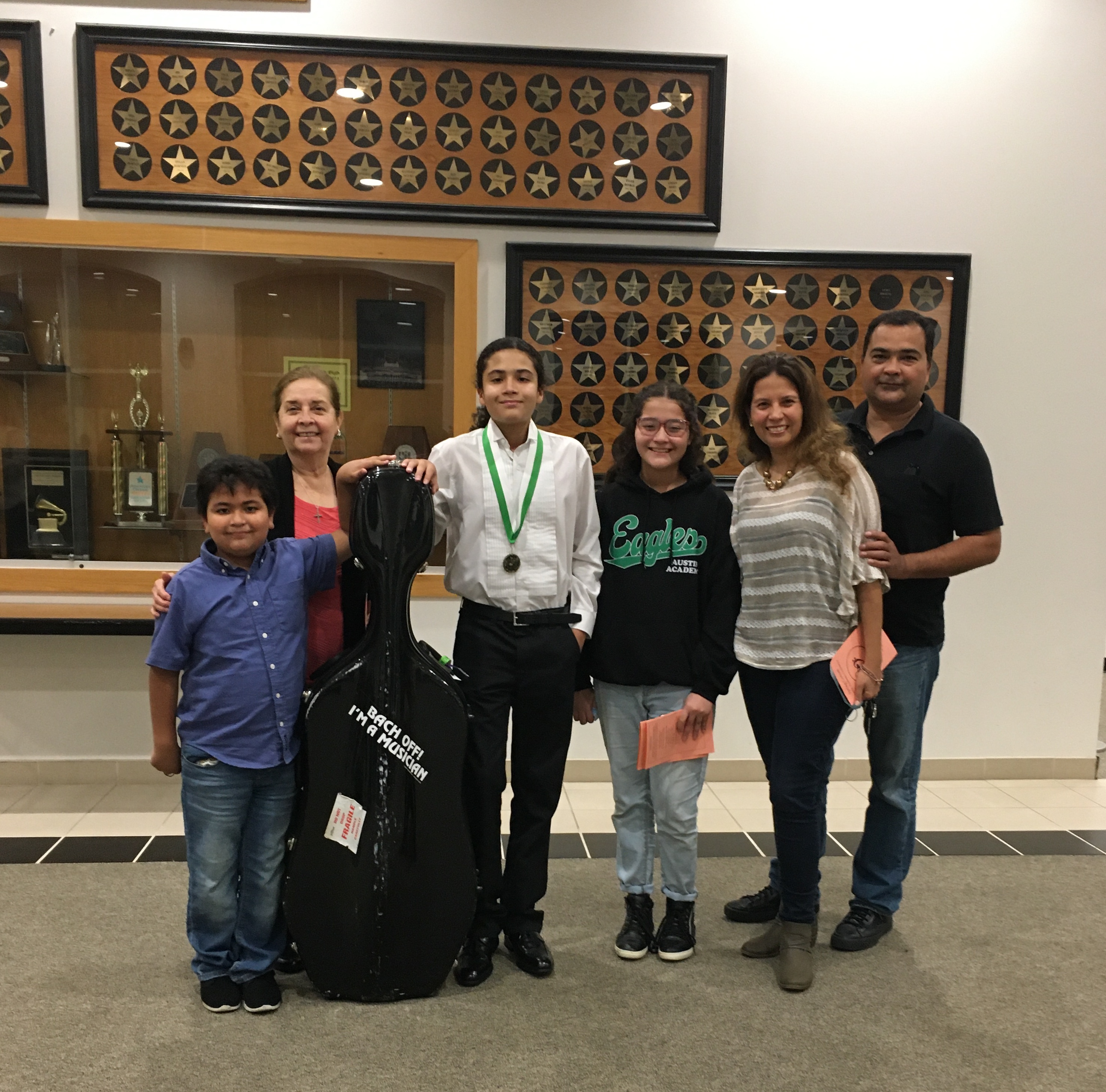 a Hispanic family stands together while a young male holds a cello case