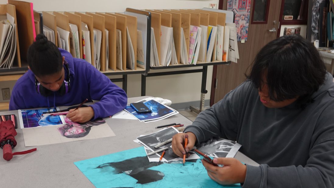 Two students sit working on their artwork