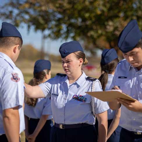 Female student conducting uniform inspection with male student beside her taking notes outside as part of the AFJROTC program at RHS.