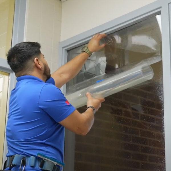 Worker installing forced-entry resistant film on a campus window.