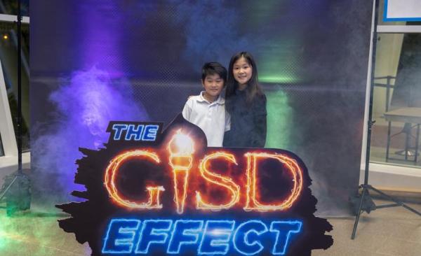An Asian boy and girl hug and smile behind The GISD Effect sign