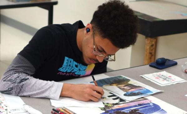Student leans over their desk working on mixed media art work.