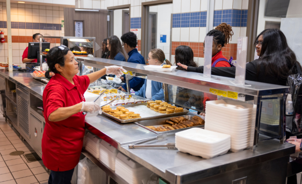 A group of students in line to receive breakfast from a cafeteria worker