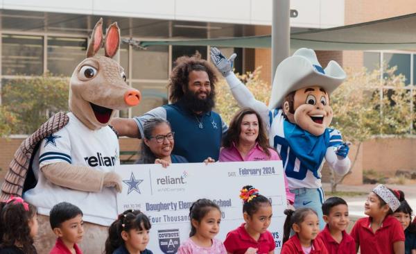 A group of children and adults posing with mascots and an oversized check.