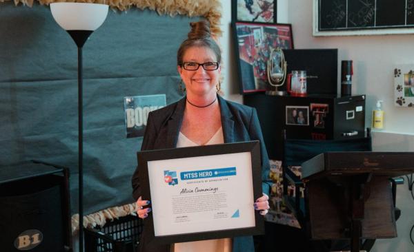 Teacher Alicia Cummings stands with an award certificate in her hand.