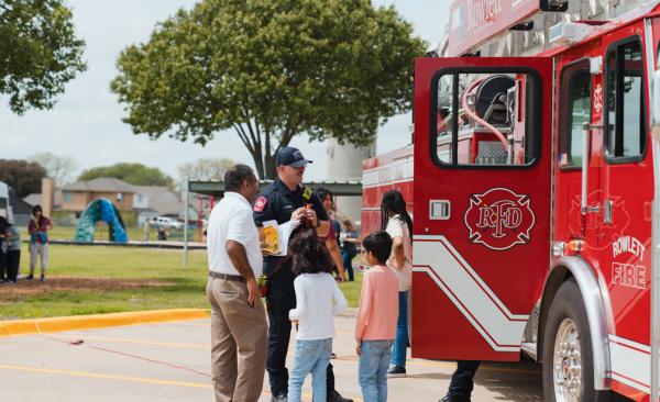 A fireman smiles while he talks with a family beside a Rowlett FD Fire Truck.