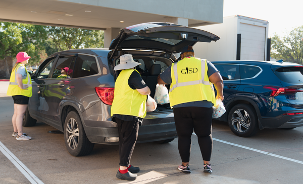 Three employees load bagged lunches into the trunk of an SUV