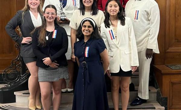 Seven speech and debate students and their coach stand staggered on a staircase