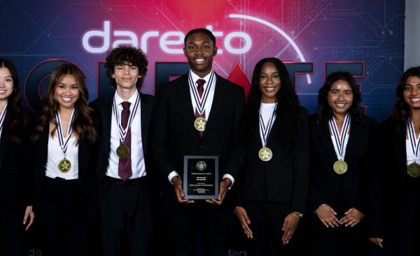 seven studens stand smiling while the middle student holds a plaque