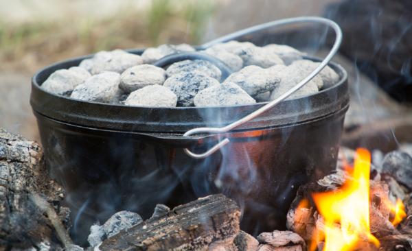 A Dutch oven with coals cooking over an outdoor fire.