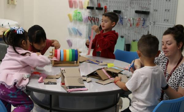 Four students and one teacher play with various items while sitting at a table