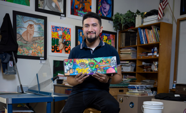 Ivan Puga posing in his classroom, holding his art booklet. 