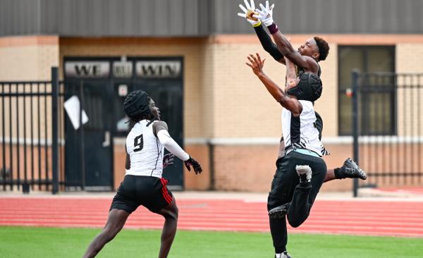 One football player jumps to catch the ball while two others try to block it.