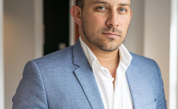 A man stands posing in a blue suit jacket looking at the camera