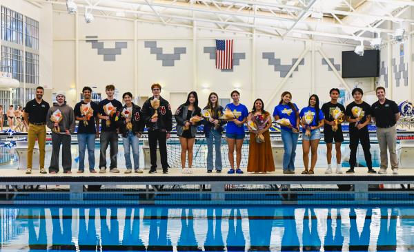 A large group of students hold flowers standing next to a pool
