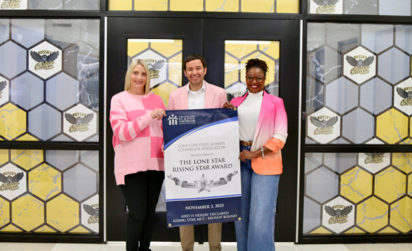 A trio of counselors stand with a banner