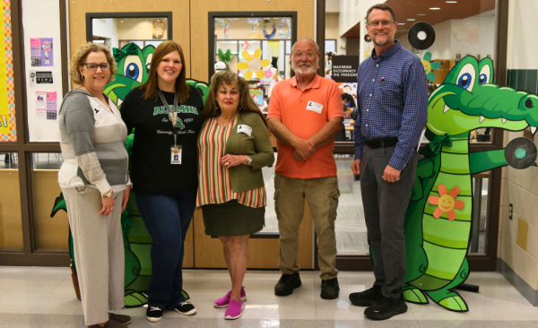 three adult women and two adult men stand together in front of an alligator cutout