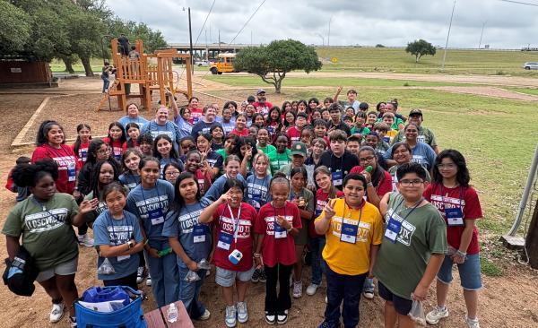 students stand at a park posing in a group, smiling