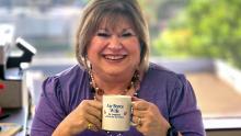 A smiling woman at a desk holding a mug that says "Air Force wife".