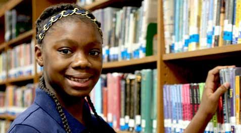 A girl smiling and taking a book of a shelf.