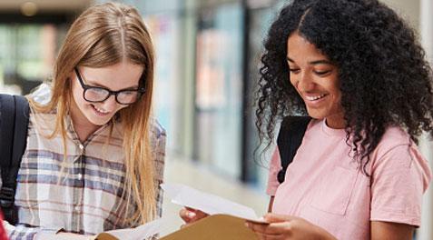 A Caribbean-American student looking at papers with another student in the hallway.