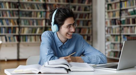 A Jewish-American student smiling while working on his computer at the library.
