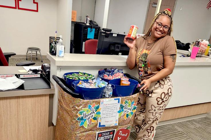 A district leader smiling and posing with a treat cart decorated with thank-yous to substitutes.