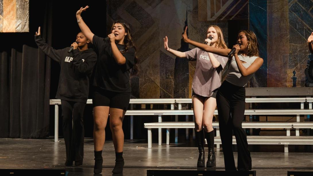 RHS students sing a song from the musical, "Six", their hands raised in the air.