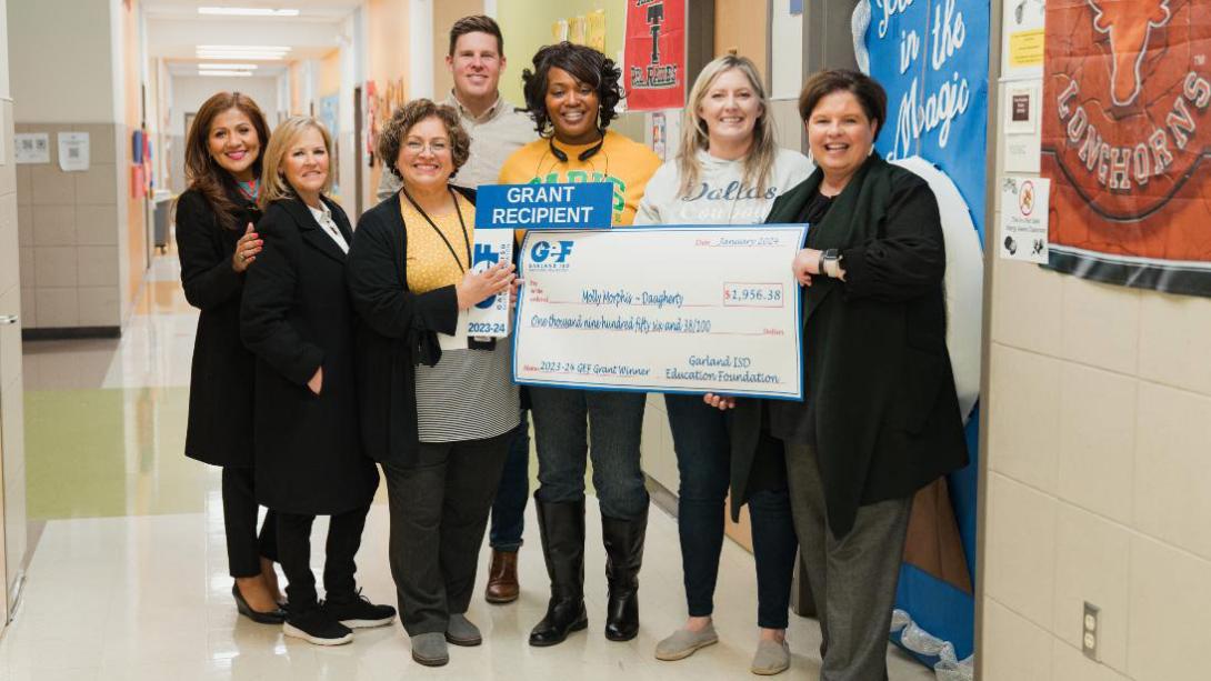 Several Daugherty teachers smile and hold a giant check in a school hallway for one of the elementary teachers.