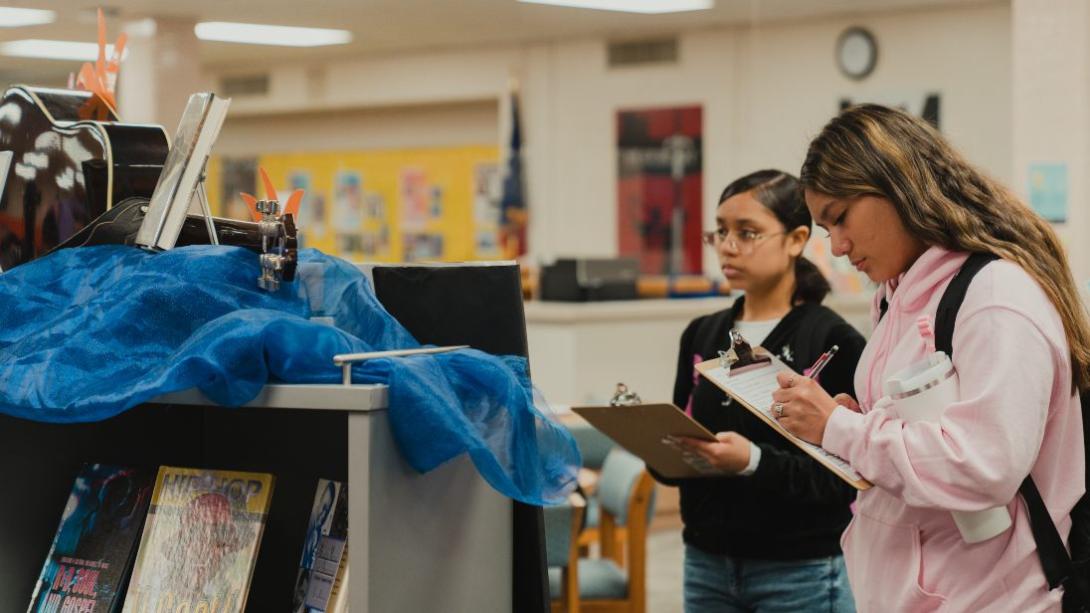 Two students hold clipboards while looking at a guitar display