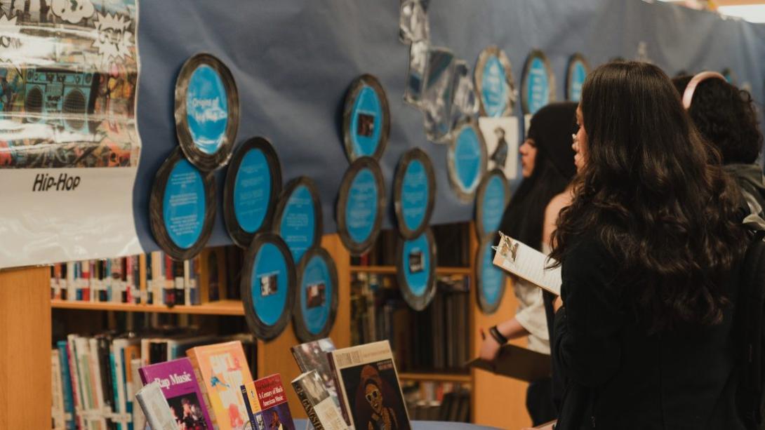 A group of students looks at a display about hip hop in the library.