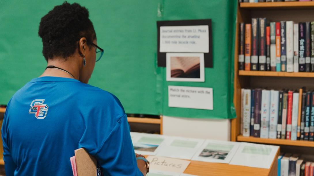 Teacher facing away from the camera and looking down at pictures displayed.