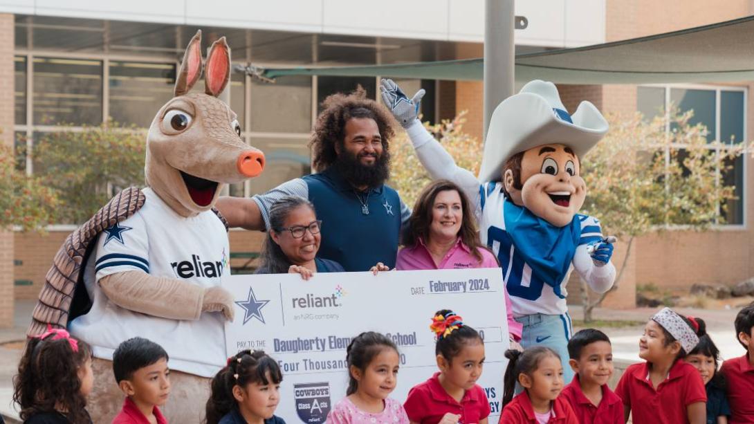 A group of children and adults posing with mascots and an oversized check.