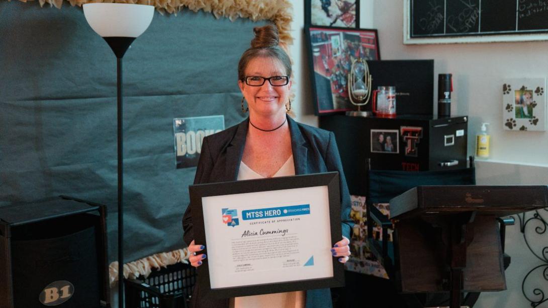 Teacher Alicia Cummings stands with an award certificate in her hand.
