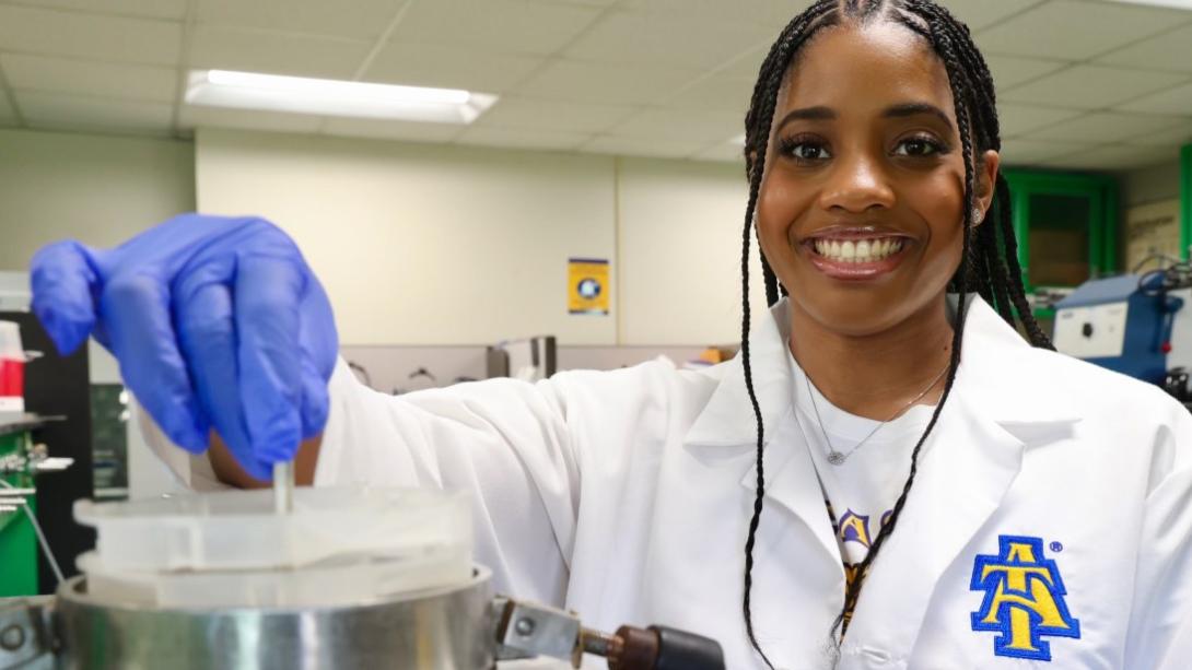Breyana Robinson poses in a white lab coat inside a laboratory.