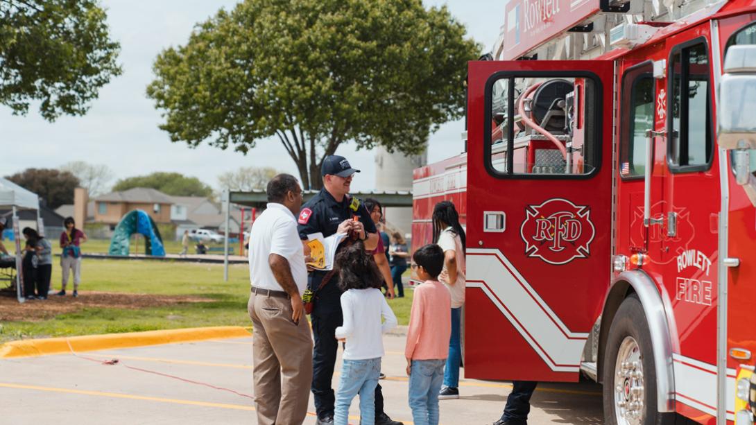 A fireman smiles while he talks with a family beside a Rowlett FD Fire Truck.