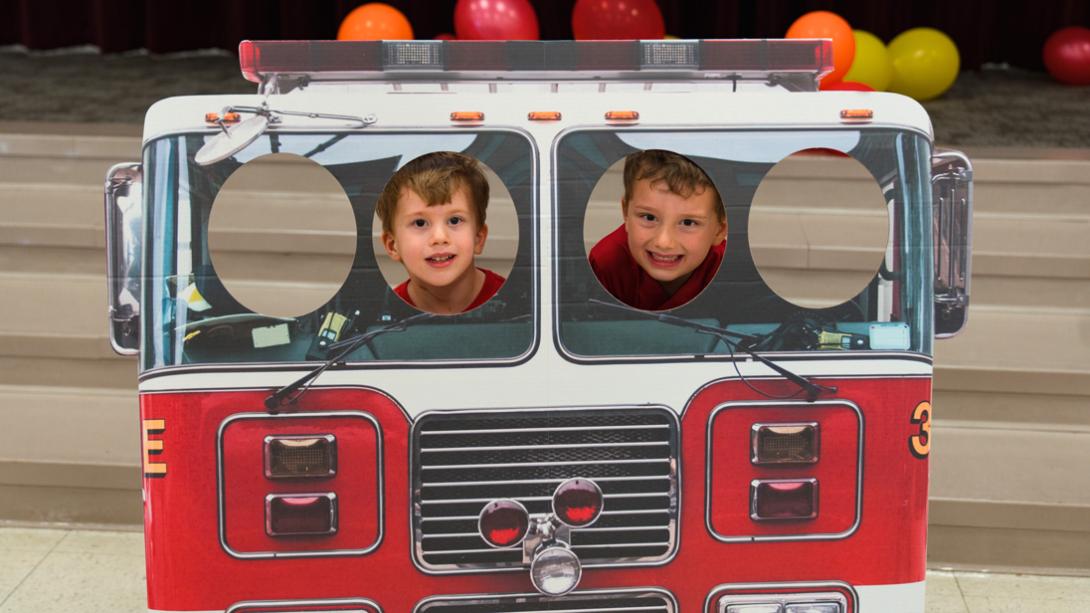 Two Herfurth ES students smile for a photo in a Firetruck cutout photo stand.