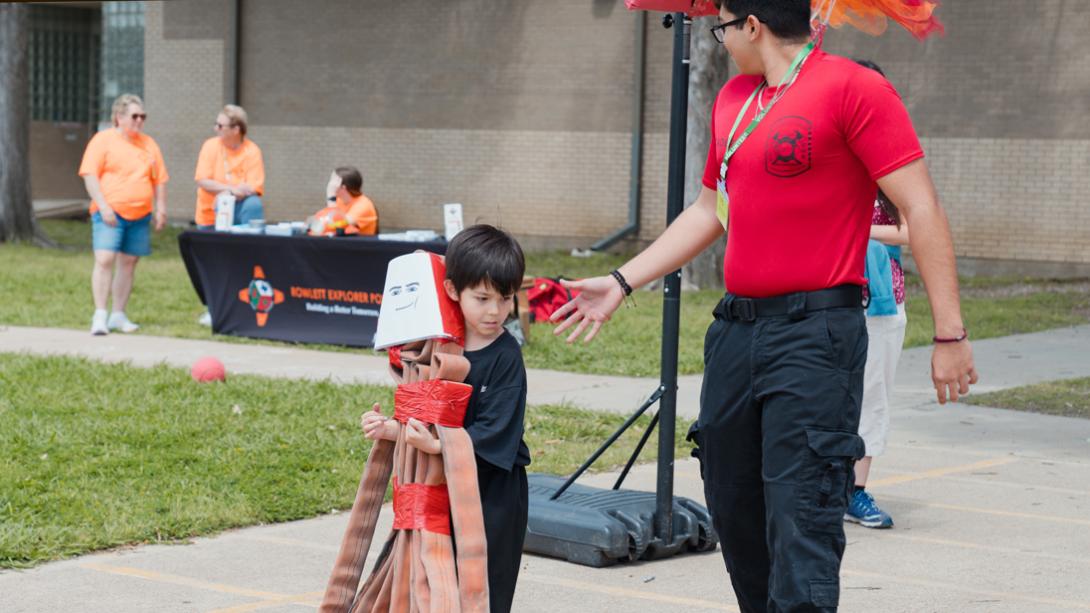 A Herfurth ES student carries a fire hose shaped like a person with a happy face, helped by a fire department member.