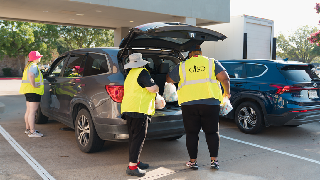 Three employees load bagged lunches into the trunk of an SUV
