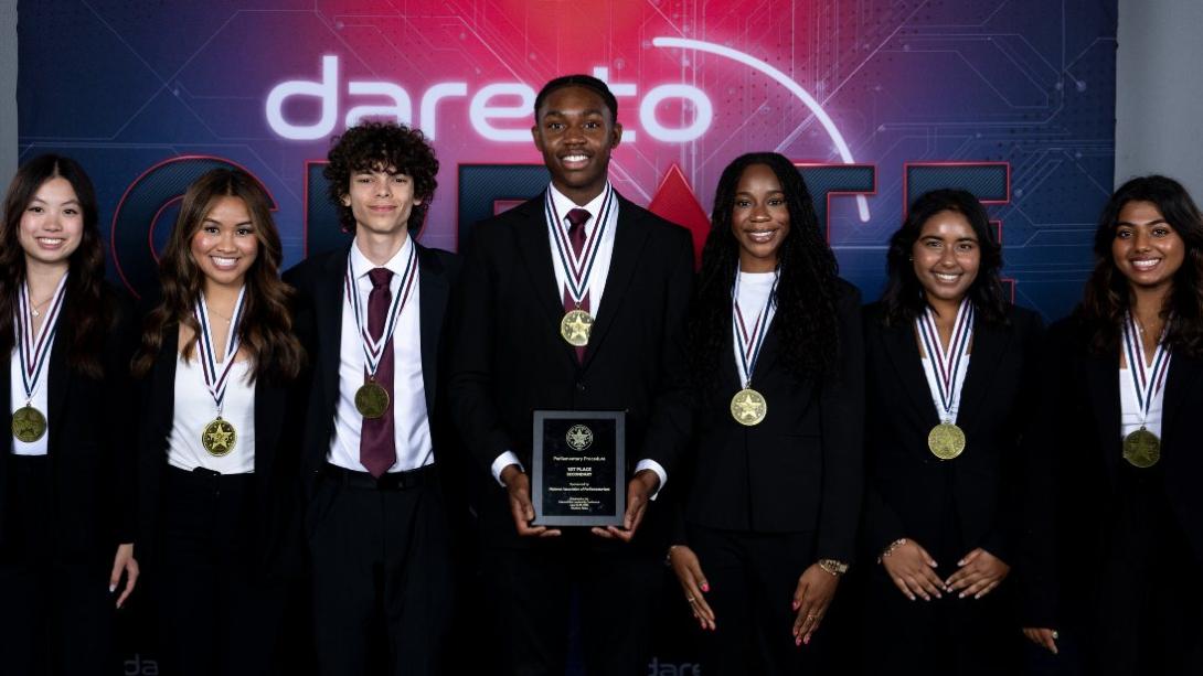 seven studens stand smiling while the middle student holds a plaque