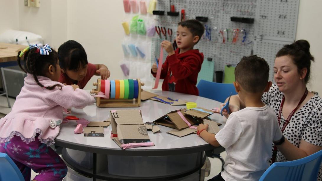 Four students and one teacher play with various items while sitting at a table