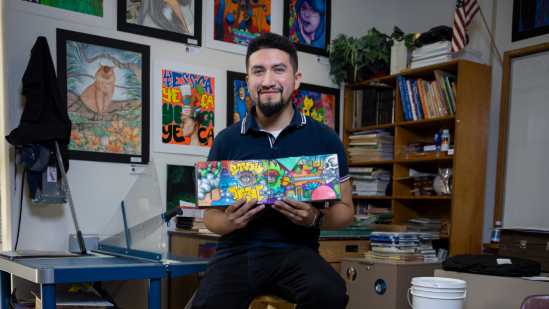 Ivan Puga posing in his classroom, holding his art booklet. 