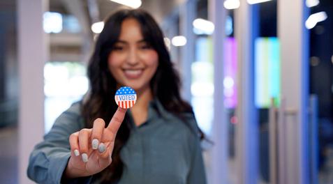 A woman holding up an "I voted" sticker on her finger while smiling.