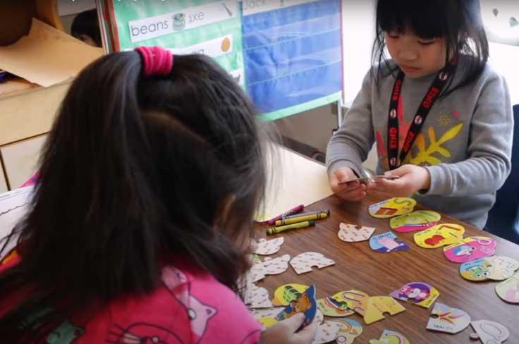 Two you girls are sorting paper cutouts in the Vietnamese Dual Language class.