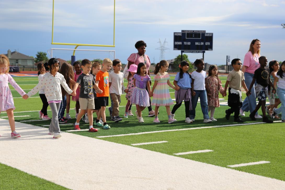 Kindergarteners walk holding hands across the field