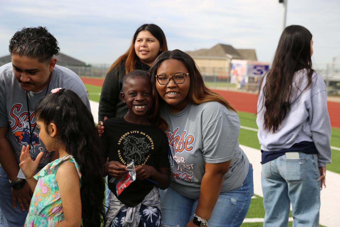 Older female student embracing younger male student and smiling at camera