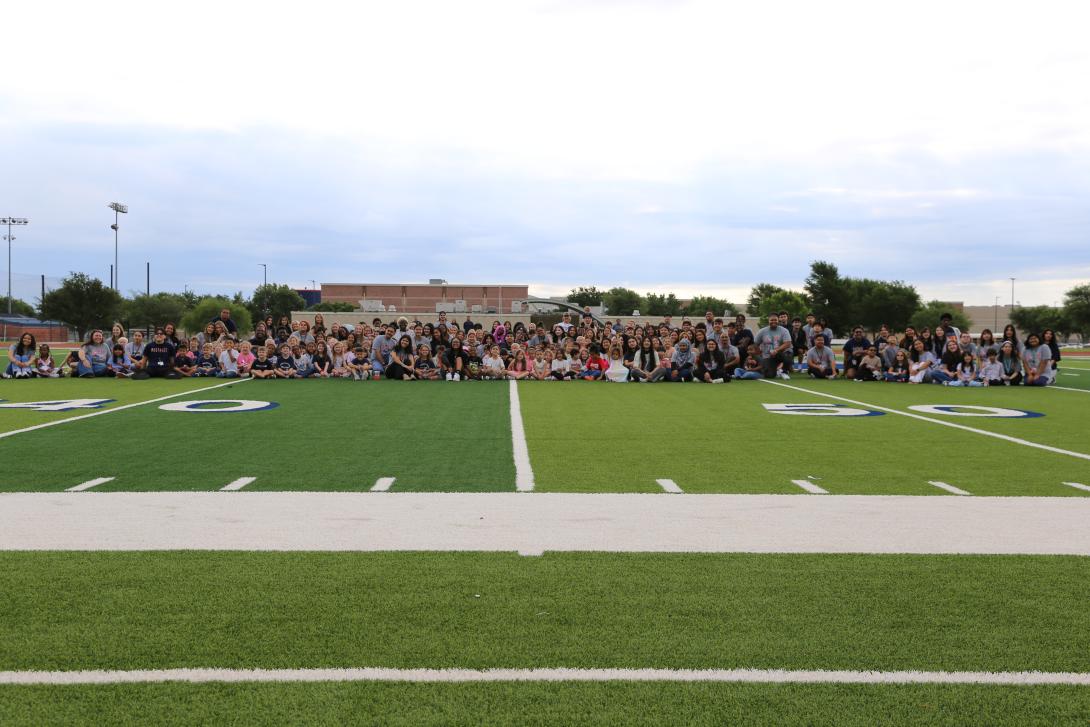 Kindergarteners and seniors sit on the football field
