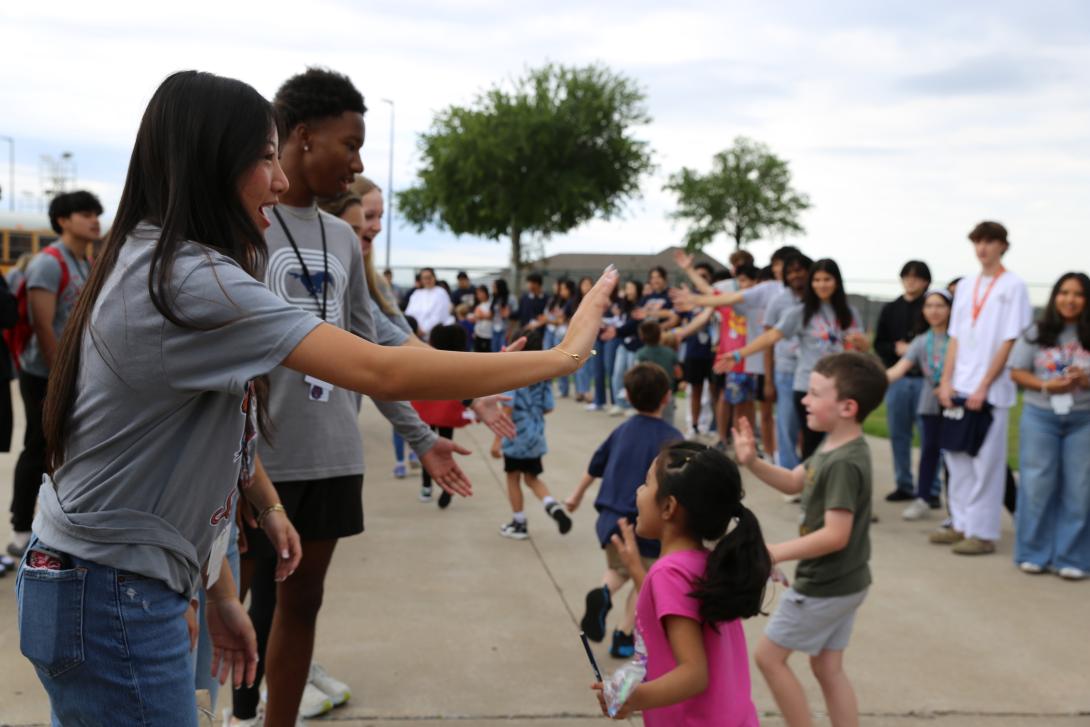 Older students give high fives to younger students as they walk by