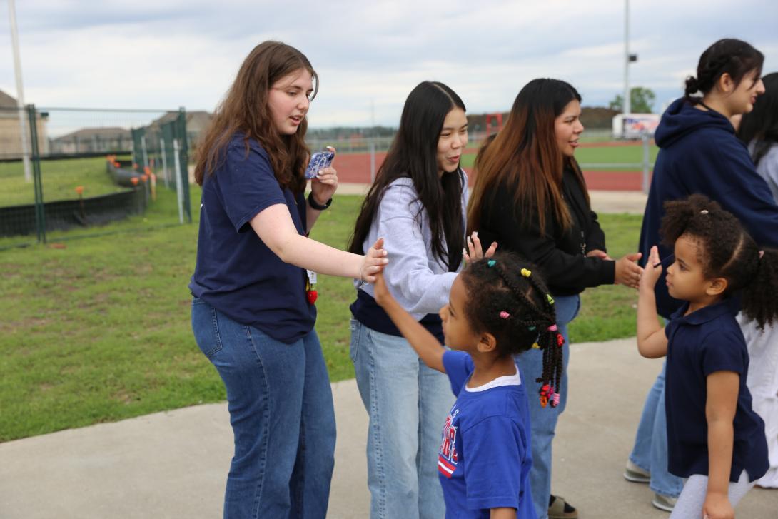 Older female students give high fives to younger students as they walk by