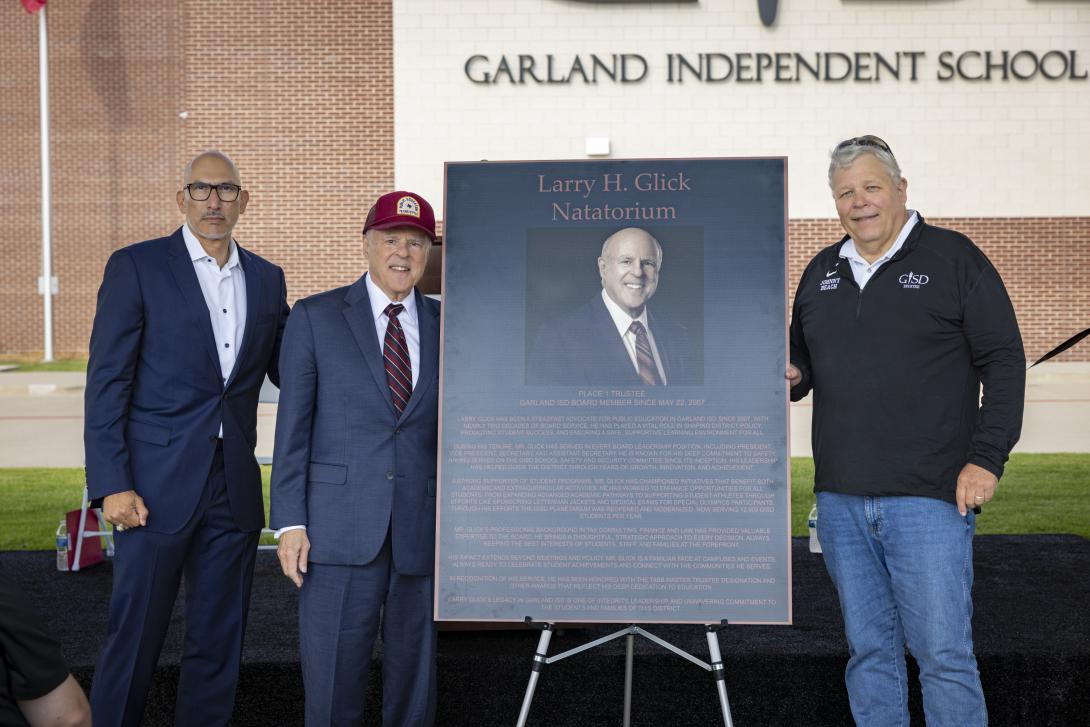Three men stand around a large commemorative plaque 
